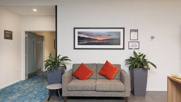 A reception area with a grey sofa, two red cushions, a framed landscape painting, and two potted plants.
