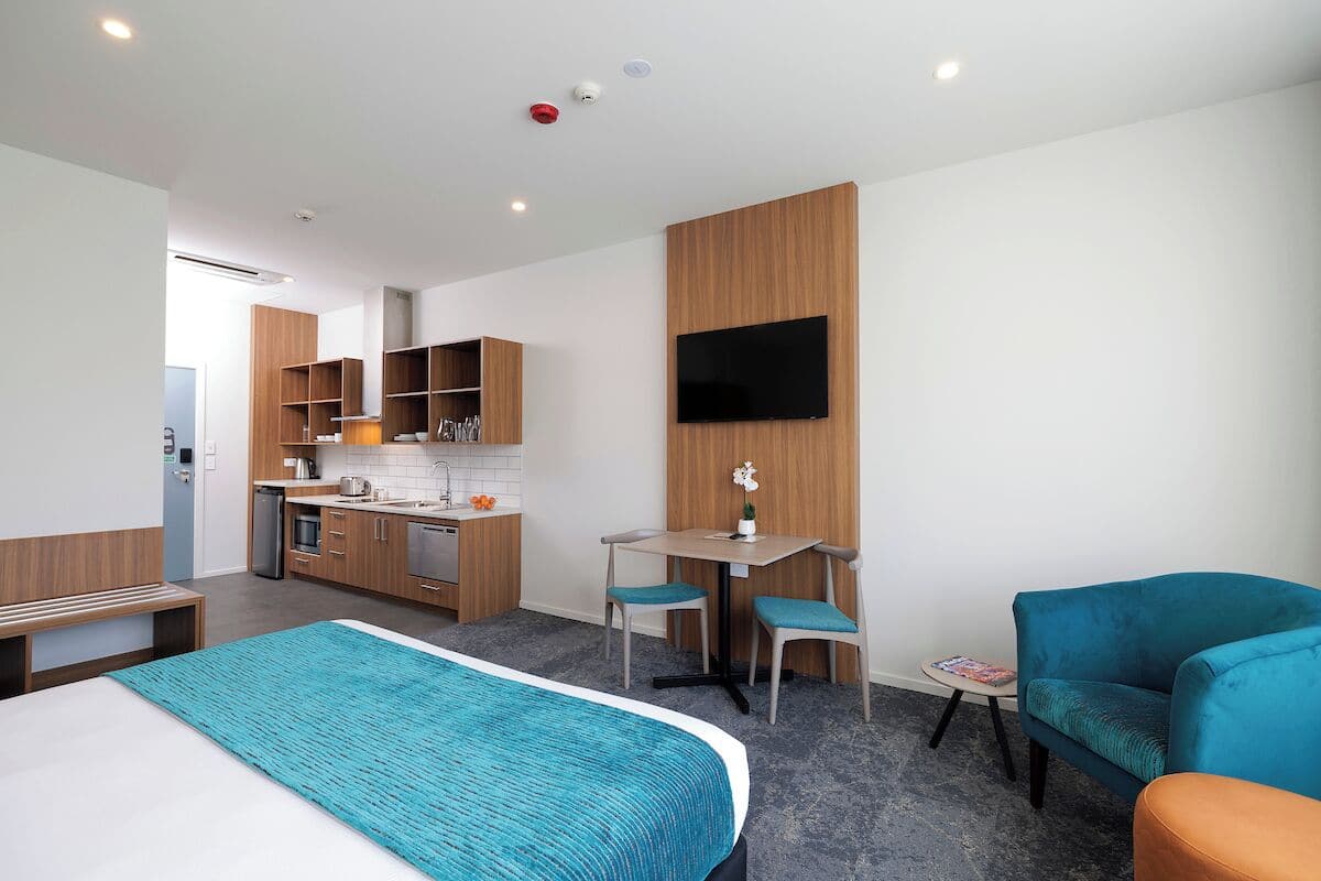 Une chambre d’hôtel moderne équipée d’un lit, d’un bureau, d’une chaise, d’un canapé, d’une télévision et d’une kitchenette.
