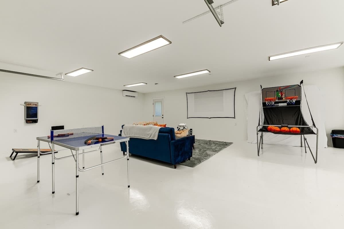 A room with a ping pong table, a blue couch, a basketball hoop, and a projector screen.