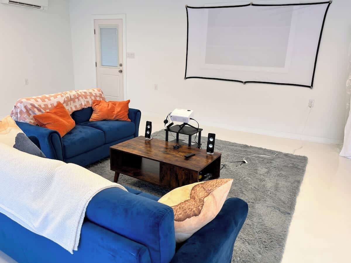 Una sala de estar con un sofá azul, una mesa de centro y una pantalla de proyector en la pared.