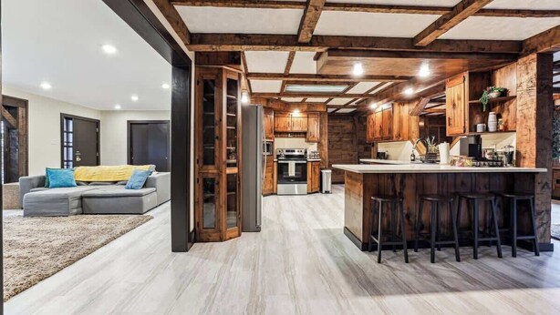 A modern kitchen with wooden beams, a bar area with stools, and a grey sofa in the living area. - Luxury Cabin*Gym*Game Room*Fireplace (Lehighton)