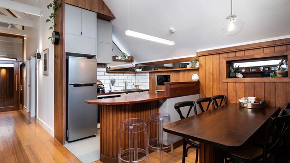 A modern kitchen with a built-in refrigerator, wooden cabinets, and a bar area with stools. - Marnies - Loft style country living (Shepherds Flat)
