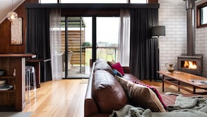 A cozy living room with a leather sofa, a fireplace, and a sliding glass door leading to a patio. - Marnies - Loft style country living (Shepherds Flat)