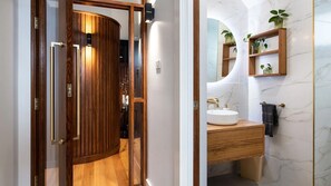 A modern bathroom with a wooden door, a white sink, marble walls, and a small shelf with plants. - Marnies - Loft style country living (Shepherds Flat)