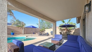 Un espacio al aire libre techado con piscina, asientos acolchados azules y una mesa de patio.