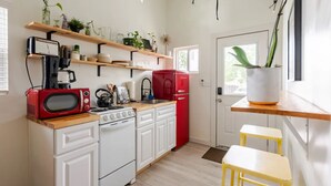 A kitchen with white cabinets, a red microwave, a red refrigerator, and wooden shelves with plants. - Charming Tiny Home Retreat!  (Austin)