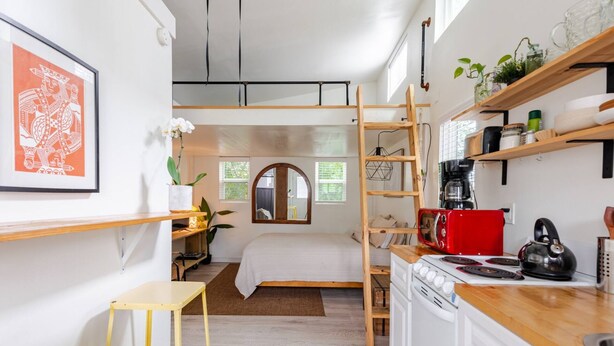 A compact kitchen with a red toaster, a kettle, and a coffee maker. There is a wooden ladder shelf above the stove and a small yellow stool in the corner. - Charming Tiny Home Retreat!  (Austin)