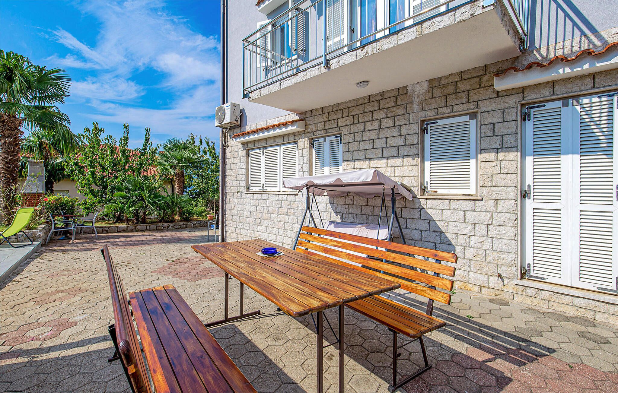 A patio with a wooden table and bench, a covered seating area, and a stone building with shutters.