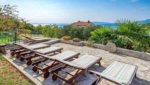 Un patio de piedra con sillones de madera y vista al mar.