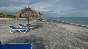 Una playa con sillas de descanso y una sombrilla de paja.