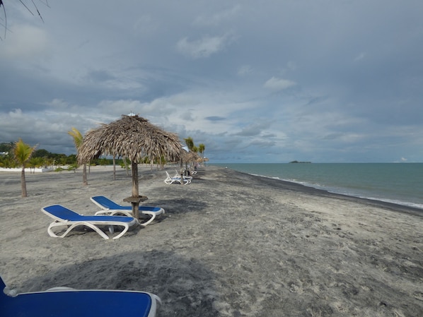 A beach with lounge chairs and a thatched umbrella.