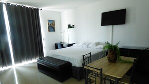 A hotel room with a bed, a desk, a chair, a TV, and a window with curtains.