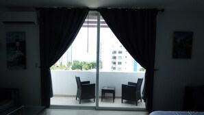 A hotel room with a balcony, a bed, a small table, two chairs, and a sofa.