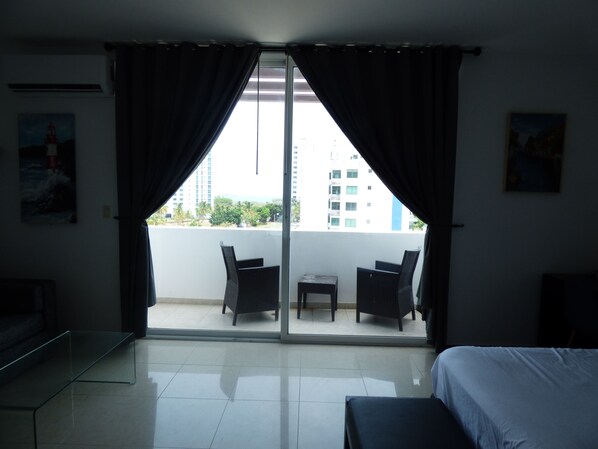 A hotel room with a balcony, a bed, a small table, two chairs, and a sofa.