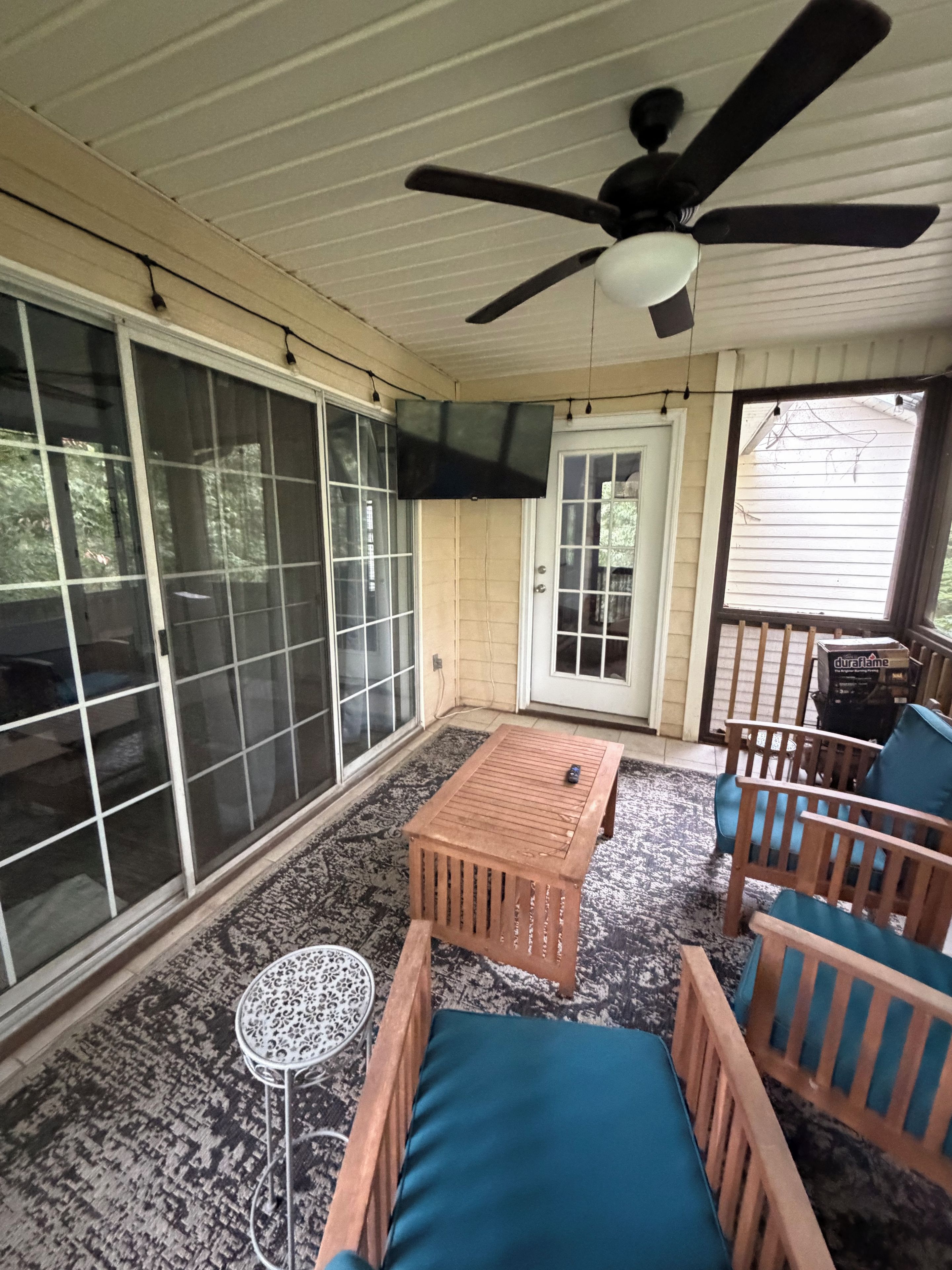 A covered patio area with a ceiling fan, a wooden table, two chairs with cushions, and a small round table with a patterned top.