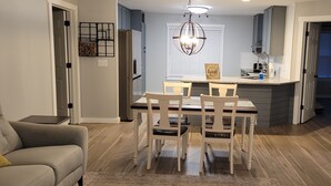 Une cuisine moderne avec un coin repas, comprenant un îlot central, un éclairage suspendu et une vue sur le salon adjacent.