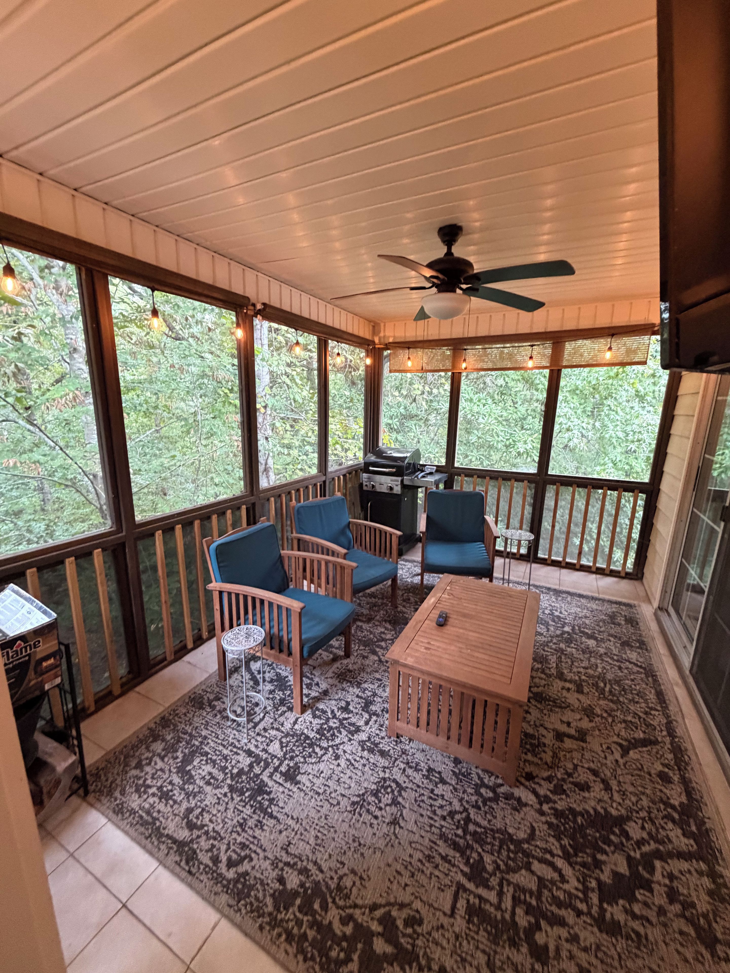A covered outdoor seating area with wooden furniture, a ceiling fan, and a grill.