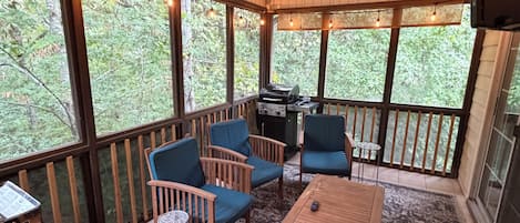 A covered outdoor seating area with wooden furniture, a ceiling fan, and a grill.