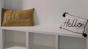 Un banc blanc avec des crochets noirs et un coussin orné du mot « Bienvenue ».