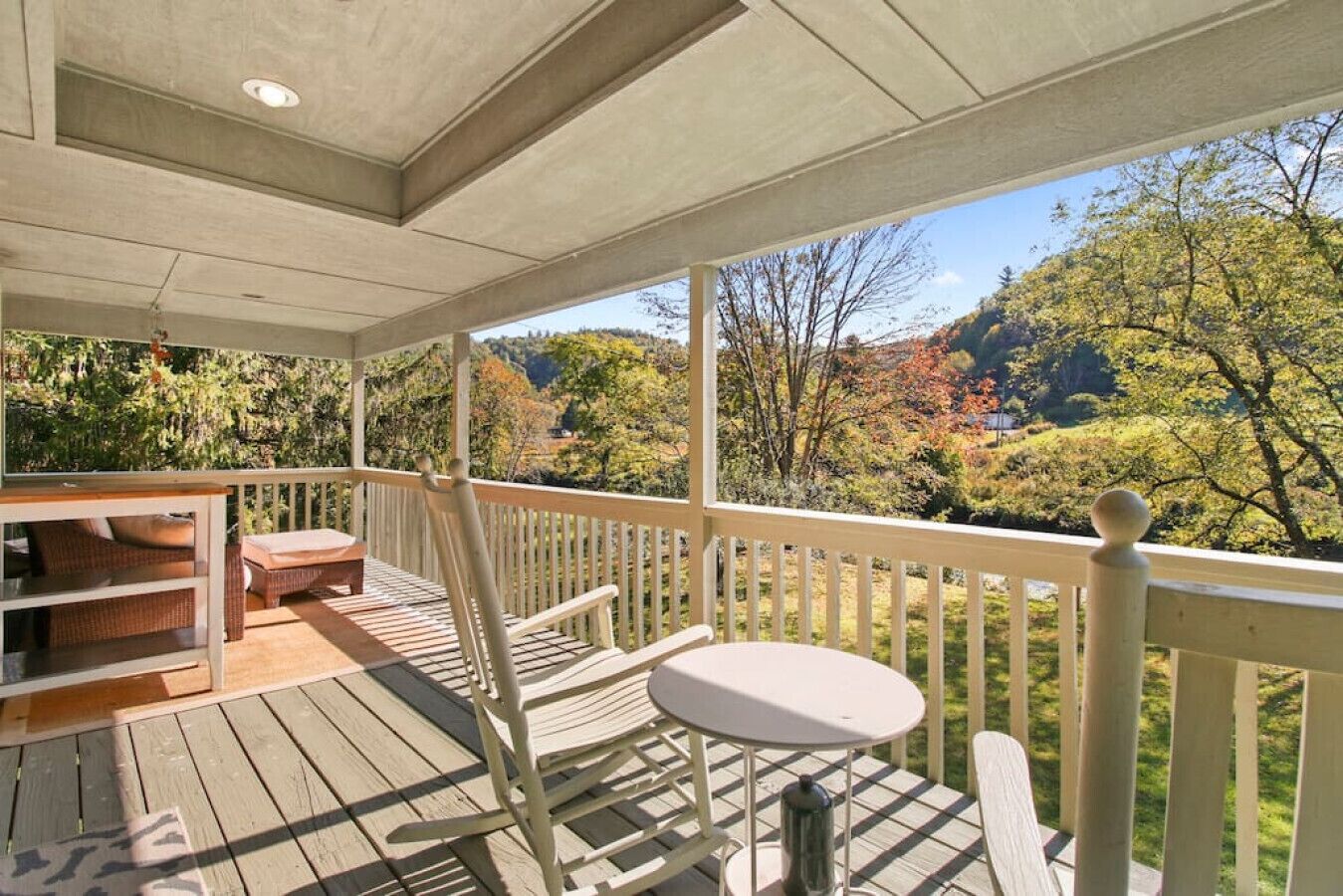 Une terrasse en bois avec une table et des chaises, offrant une vue panoramique sur un paysage pittoresque, avec des arbres et des collines.
