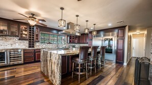 A modern kitchen with a large island, bar stools, and a ceiling fan. - Just in time for SUPER BOWL! Mansion with Luscious Strip Views! (Las Vegas)