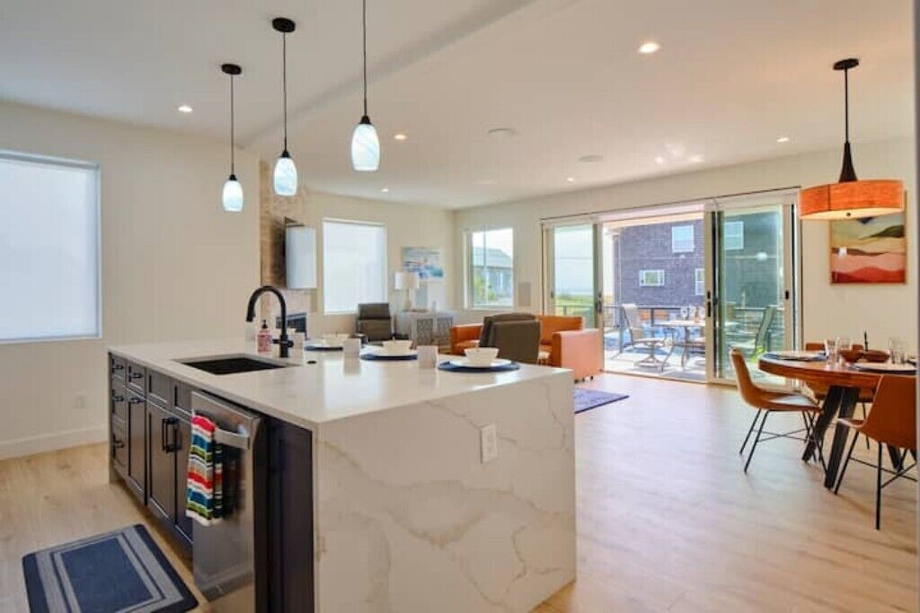 A modern kitchen with a marble island, a dining area with a table and chairs, and a large window with a view of the outside.