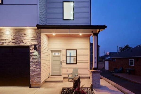 Una casa moderna de dos pisos con fachada de piedra, puerta principal y un pequeño porche con una silla.