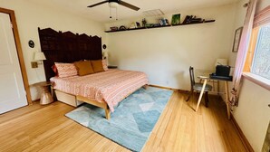 A bedroom with a bed, a desk, a chair, a ceiling fan, a window, and a bookshelf. - Honey Comb Guest Suite (shared house) (San Marcos)