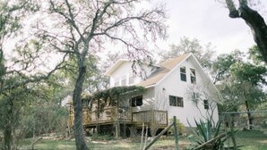 A two-story house with a wooden deck, surrounded by trees and vegetation. - Honey Comb Guest Suite (shared house) (San Marcos)