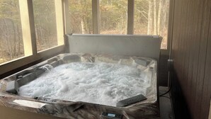 Un bain à remous doté d’un panneau de commande, entouré de grandes fenêtres donnant sur une zone boisée.
