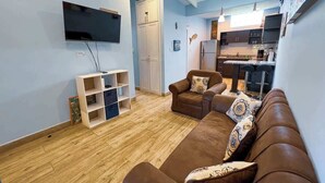 Sala de estar com sofá marrom, televisão de tela plana na parede e piso de madeira.