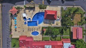 Vista aérea de um hotel com piscina, várias estruturas com telhados vermelhos e um estacionamento.