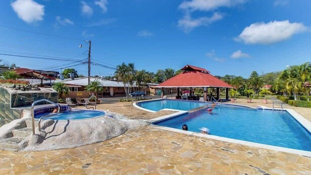 Uma área de piscina com várias piscinas, um espaço de estar coberto e um deck revestido de pedra.