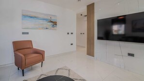 Een moderne woonkamer met een bruine leren bank, een schilderij van een zeegezicht, een flatscreentelevisie aan een witte muur en een kamerbreed tapijt met dessin.