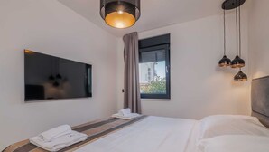 Een moderne hotelkamer met een groot bed, een flatscreen televisie aan de wand, een raam met gordijnen en een plafondlamp.