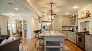Una cocina moderna con una isla central, electrodomésticos de acero inoxidable y un área de comedor con sofá y sillas grises.