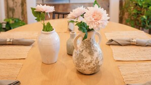Una mesa de comedor con dos jarrones de flores, una araña y vista hacia otra zona de comedor.