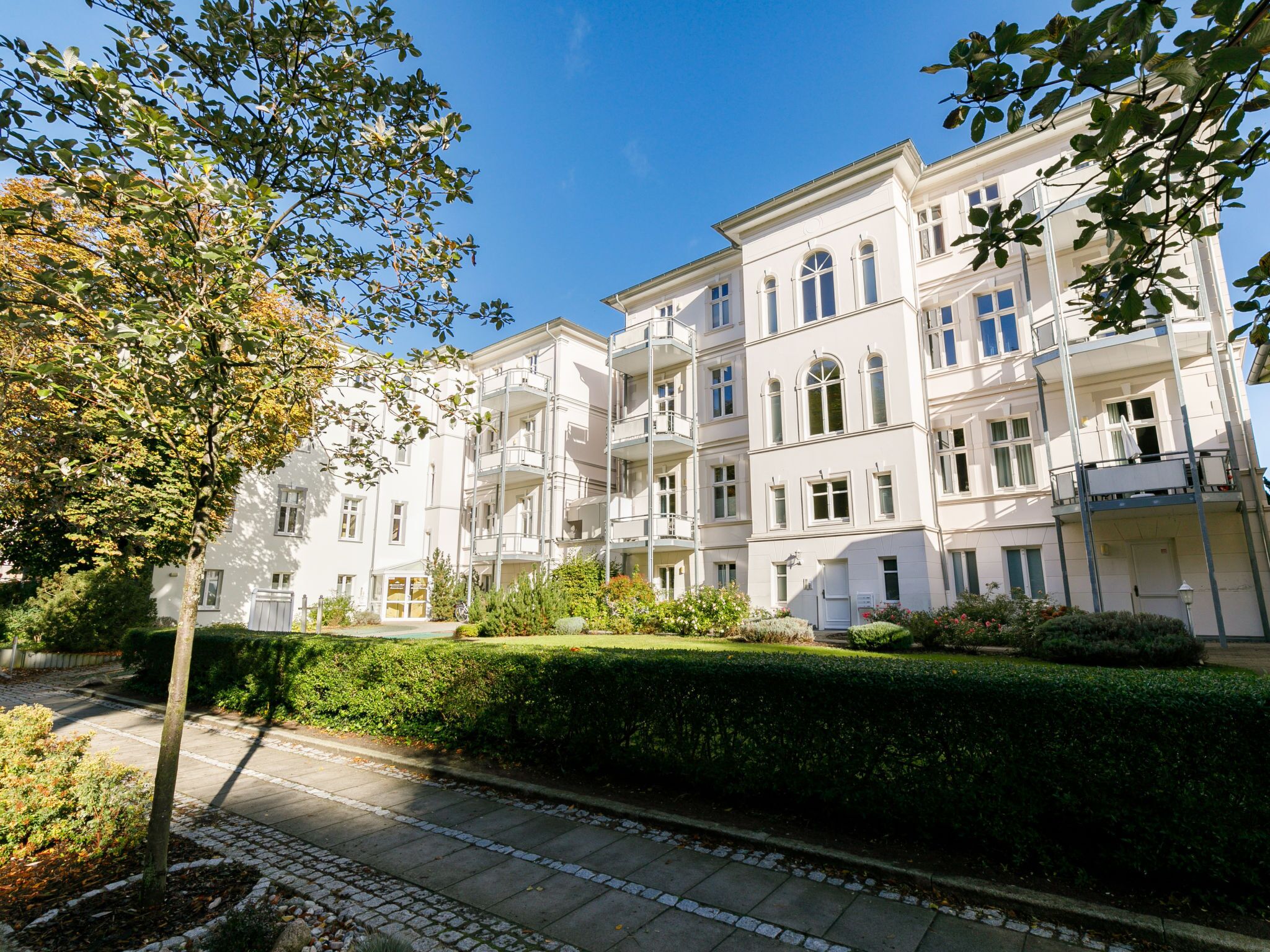 A multi-story residential building with balconies, a paved pathway, and well-maintained greenery.