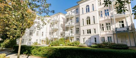 A multi-story residential building with balconies, a paved pathway, and well-maintained greenery.