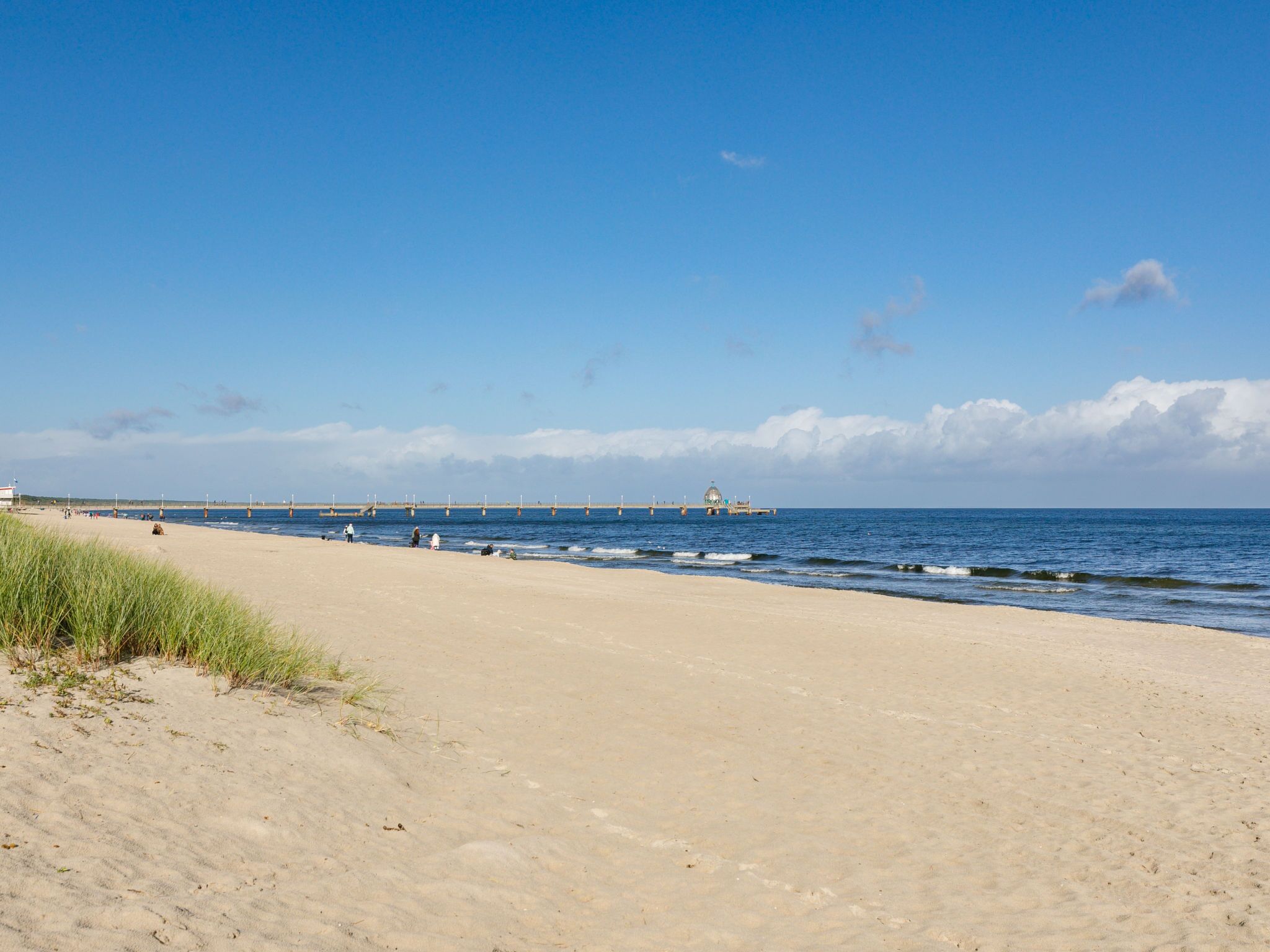 Ein Strand mit einem Steg, der ins Meer führt, mit einem kleinen Gebäude am Ende.