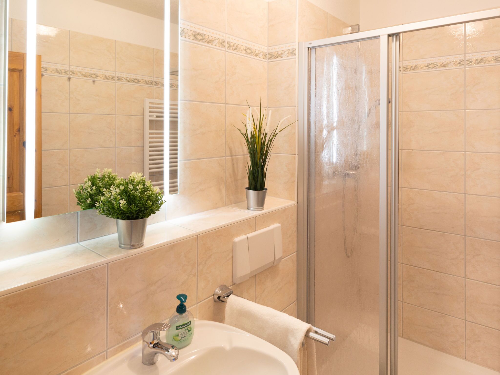 A bathroom with a sink, mirror, potted plants, and a shower area.