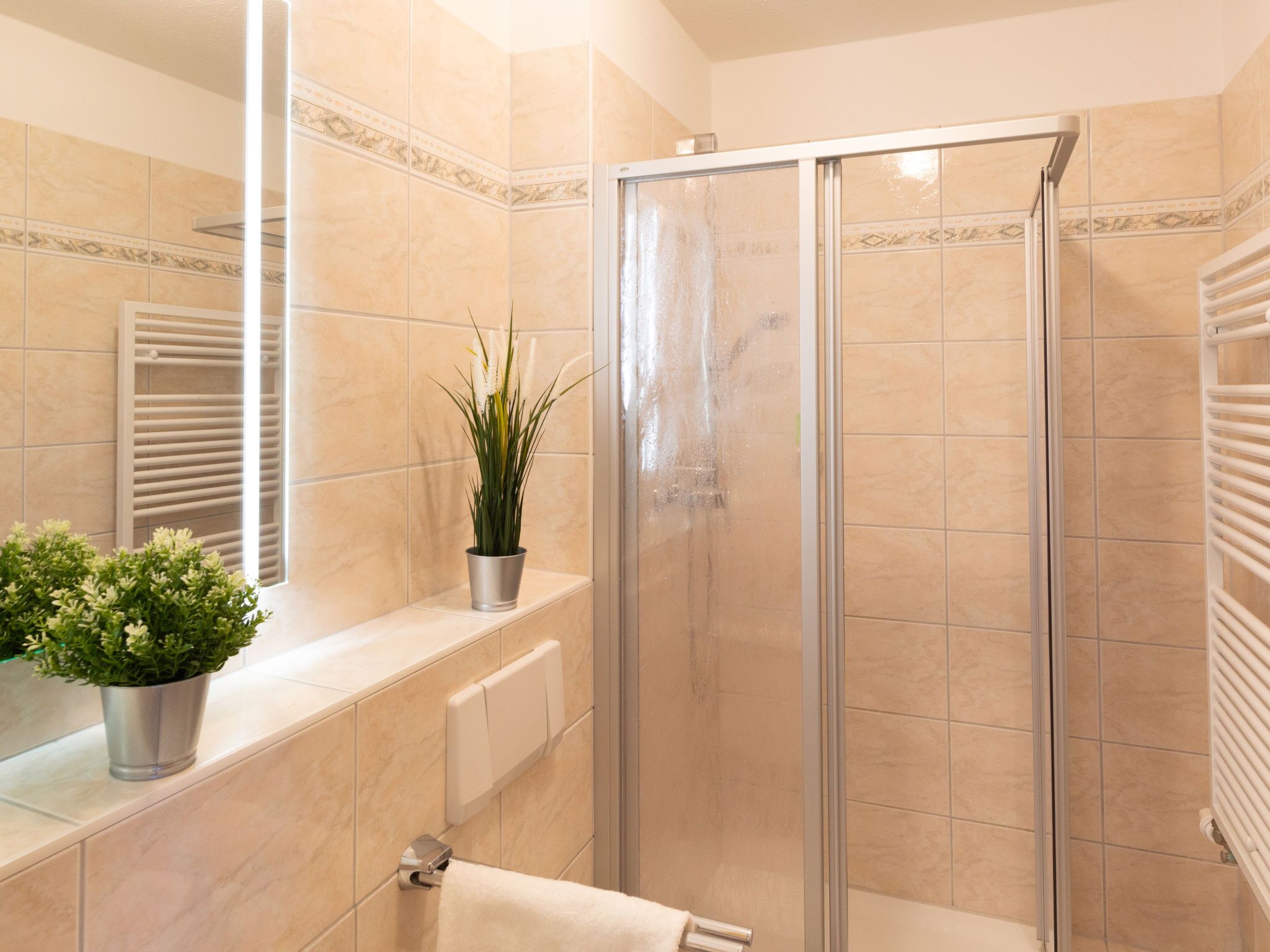 A bathroom with a glass shower enclosure, a sink with a potted plant, and a towel rack.