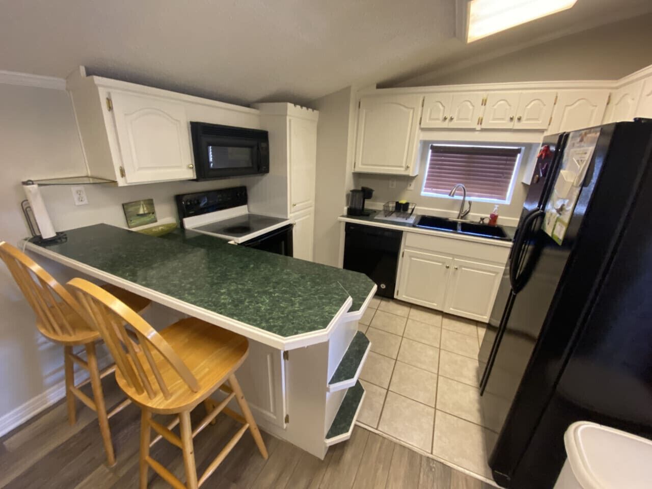 A compact kitchen with a central island, white cabinetry, a black refrigerator, and a microwave.