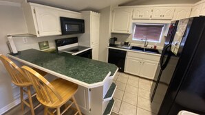 Una cocina compacta con una isla central, muebles de cocina blancos, un refrigerador negro y un microondas.