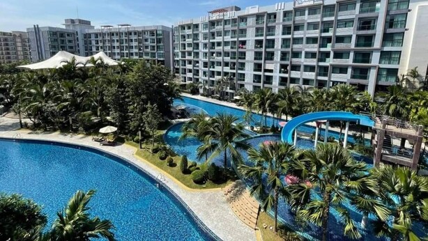 Un hotel con varios pisos, piscina y palmeras.