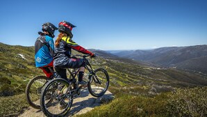 Two people on a mountain bike trail with a scenic view of hills and valleys.