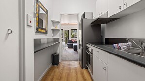 A narrow kitchen with a built-in oven, a sink, and a window overlooking a living area.