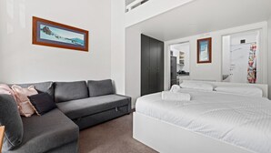 A modern hotel room with a grey sofa, a large bed, and a wardrobe.