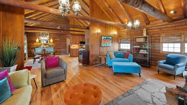 Interior de una cabaña de madera con techo de madera, comedor, sala de estar con sofás azules y área de cocina.