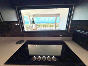 A kitchen with a built-in stove and a large window overlooking a balcony with a view of the sea. - Endless ocean views and pool, by El Yunque. (Río Grande)